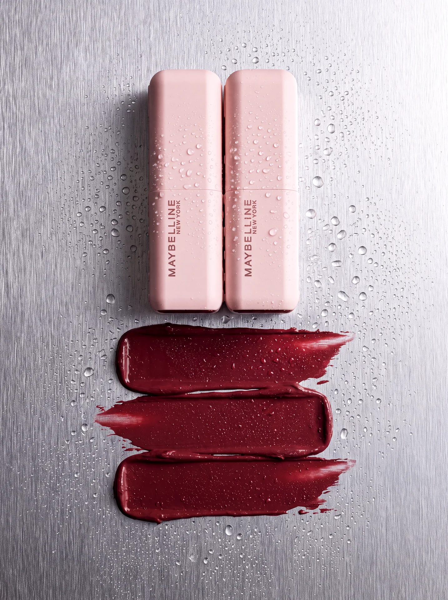 Top view product composition with two pale pink cosmetic objects, red texture and water drops on metal