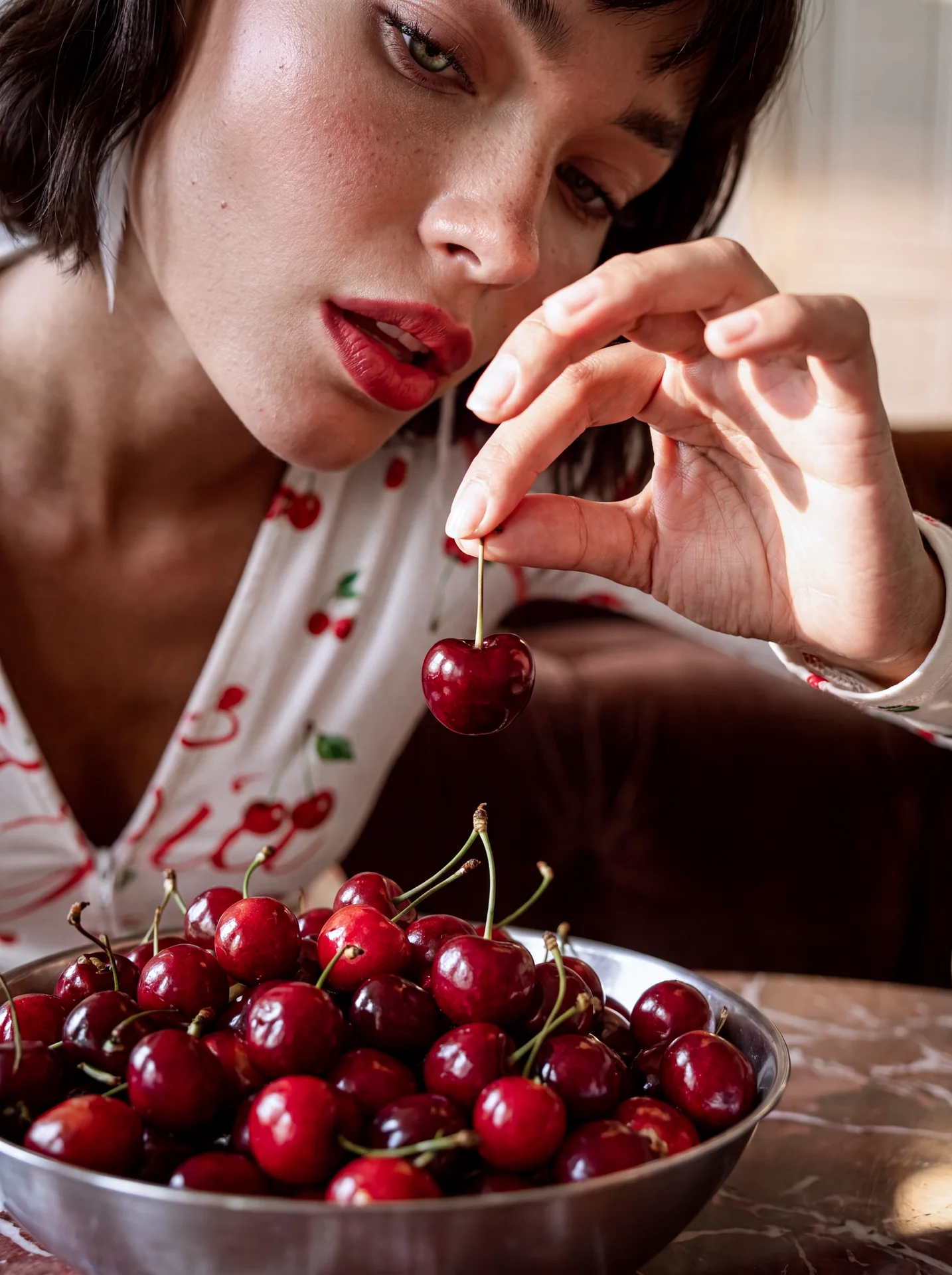 Close-up of a model holding a cherry above a bowl while wearing a white cherry-print outfit