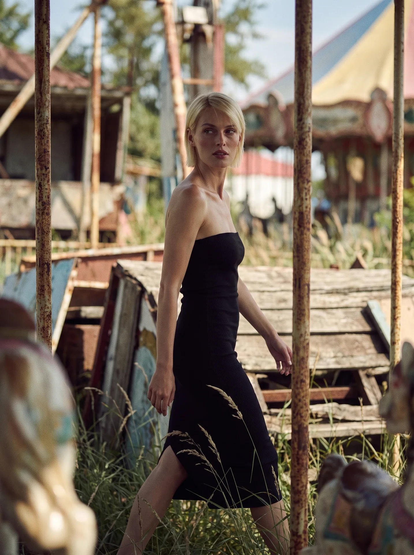 Blonde model in a black dress walking between rusted fairground structures