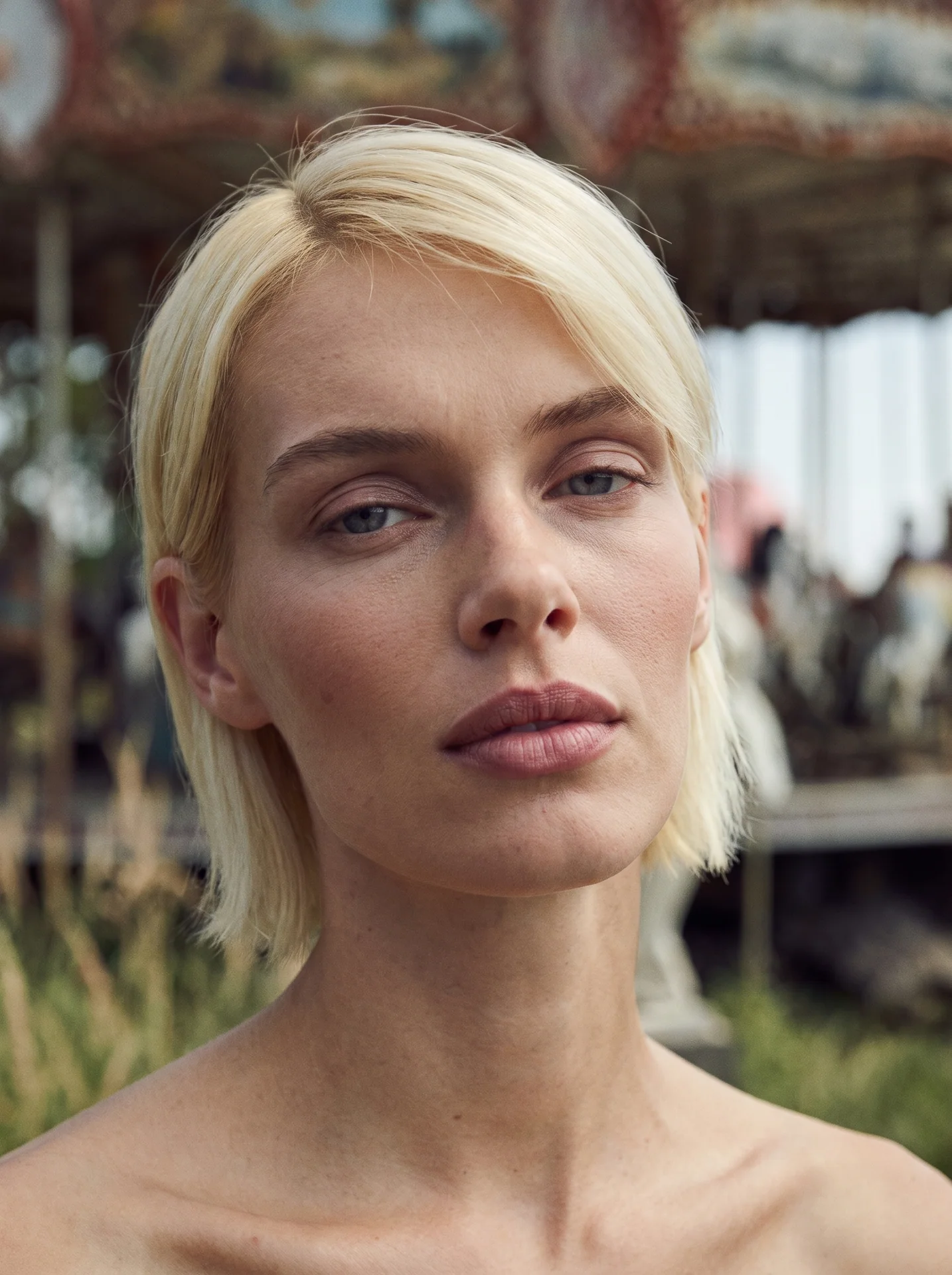 Close portrait of a blonde model with soft daylight and a blurred fairground behind her