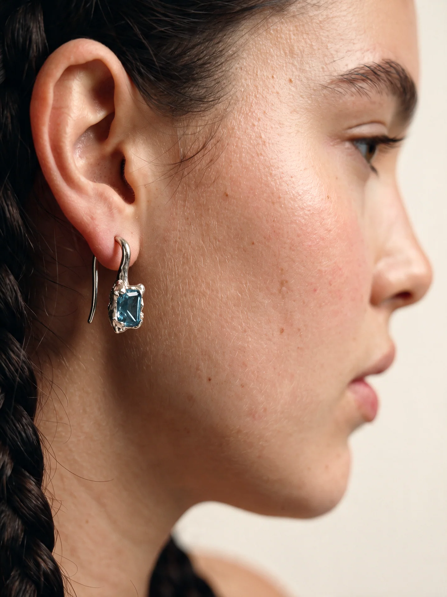Profile close-up of a model wearing a silver-toned earring with a blue centerpiece
